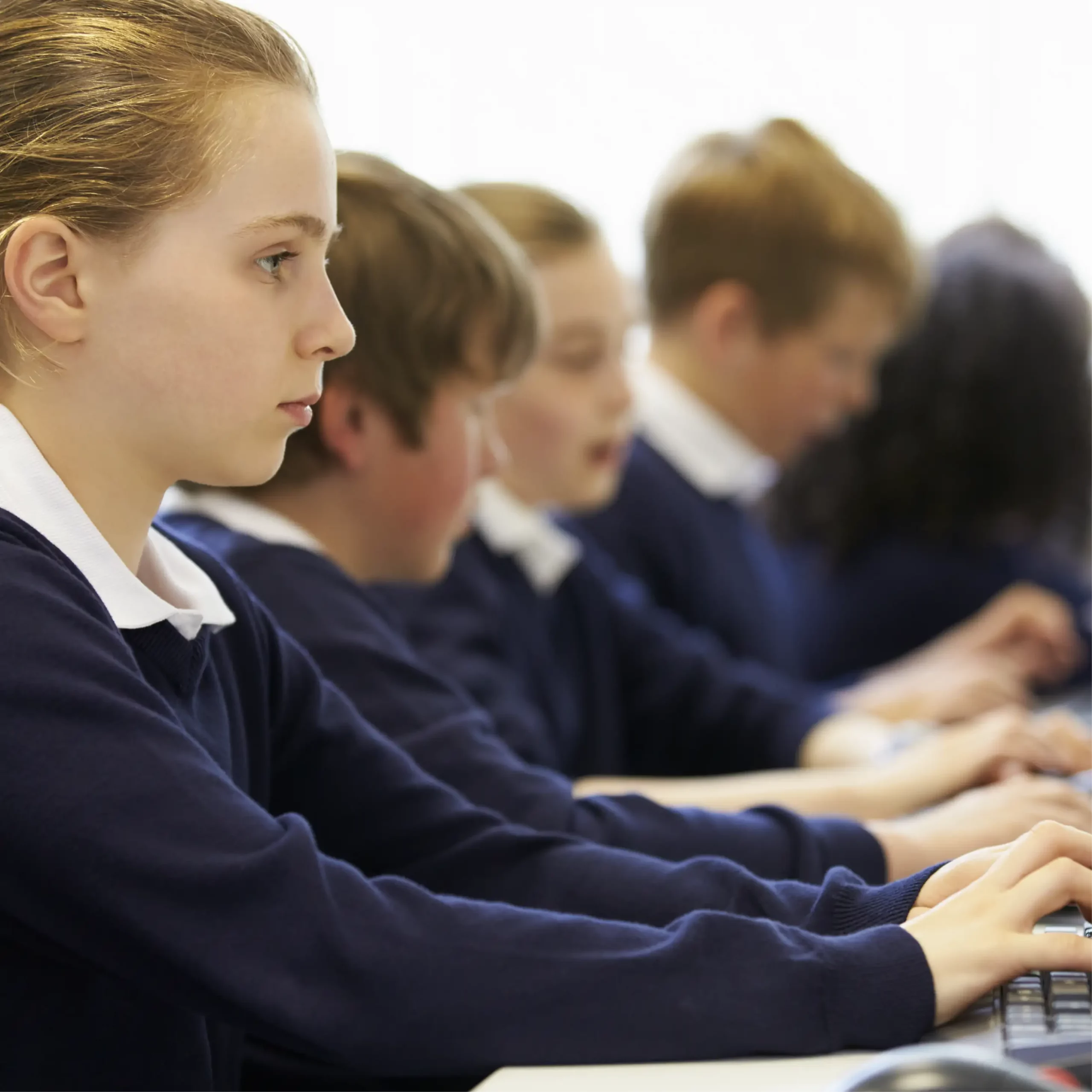 A row of pupils wearing blue uniform type on computers.