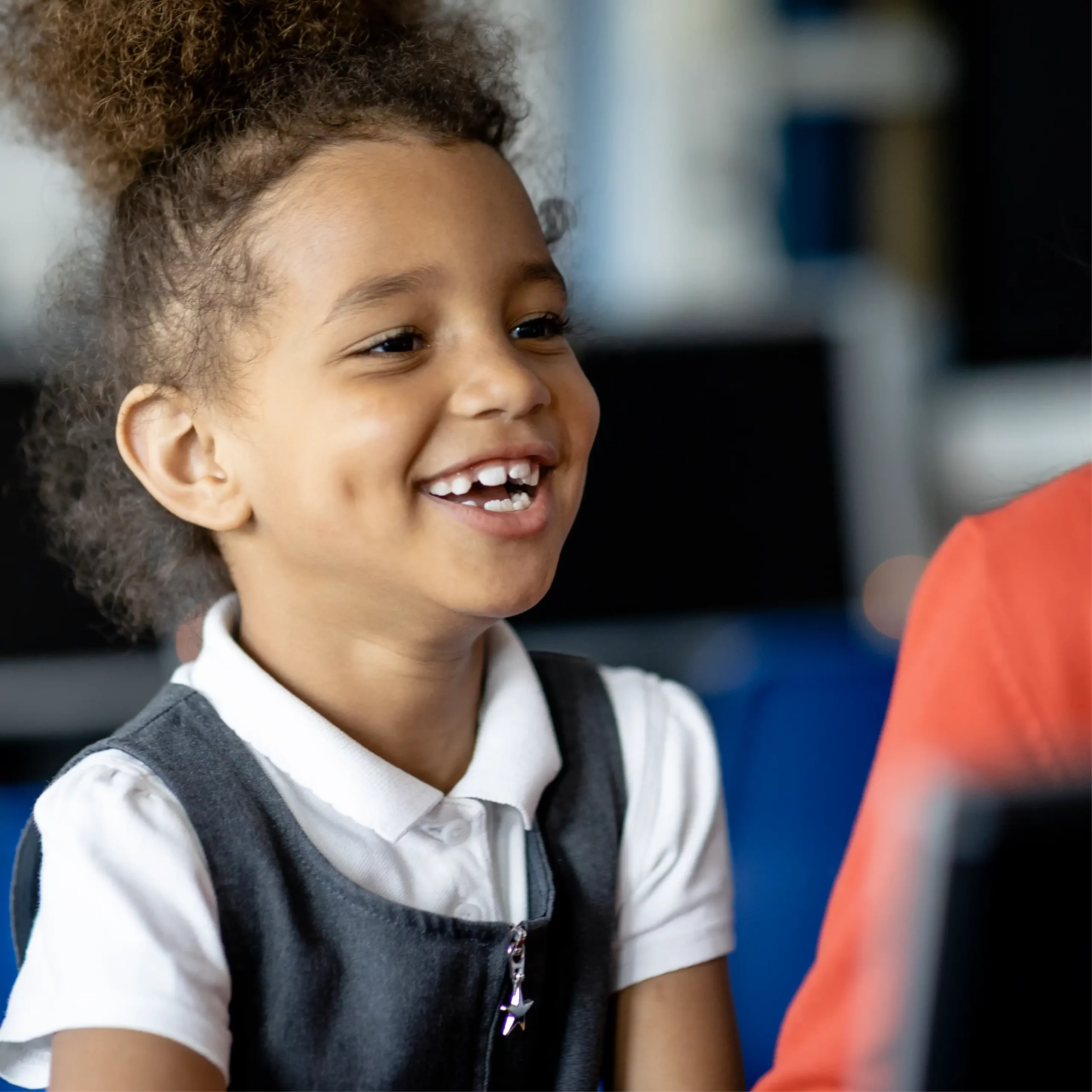 A happy girl wearing grey school uniform sits in a classroom.