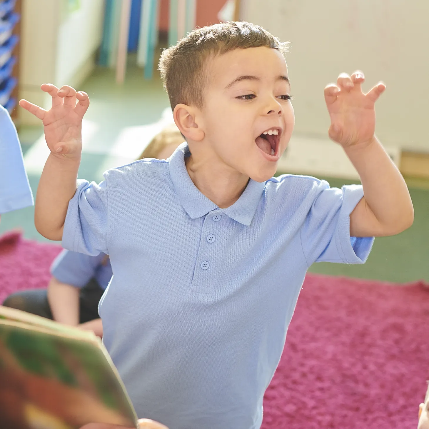 Young boy in a blue polo shirt acting out a story with his hands raised like claws and mouth open wide.