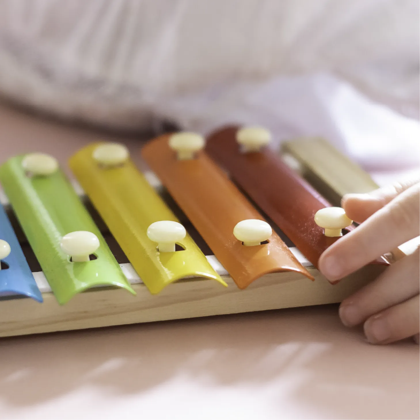A hand touches a rainbow coloured xylophone.