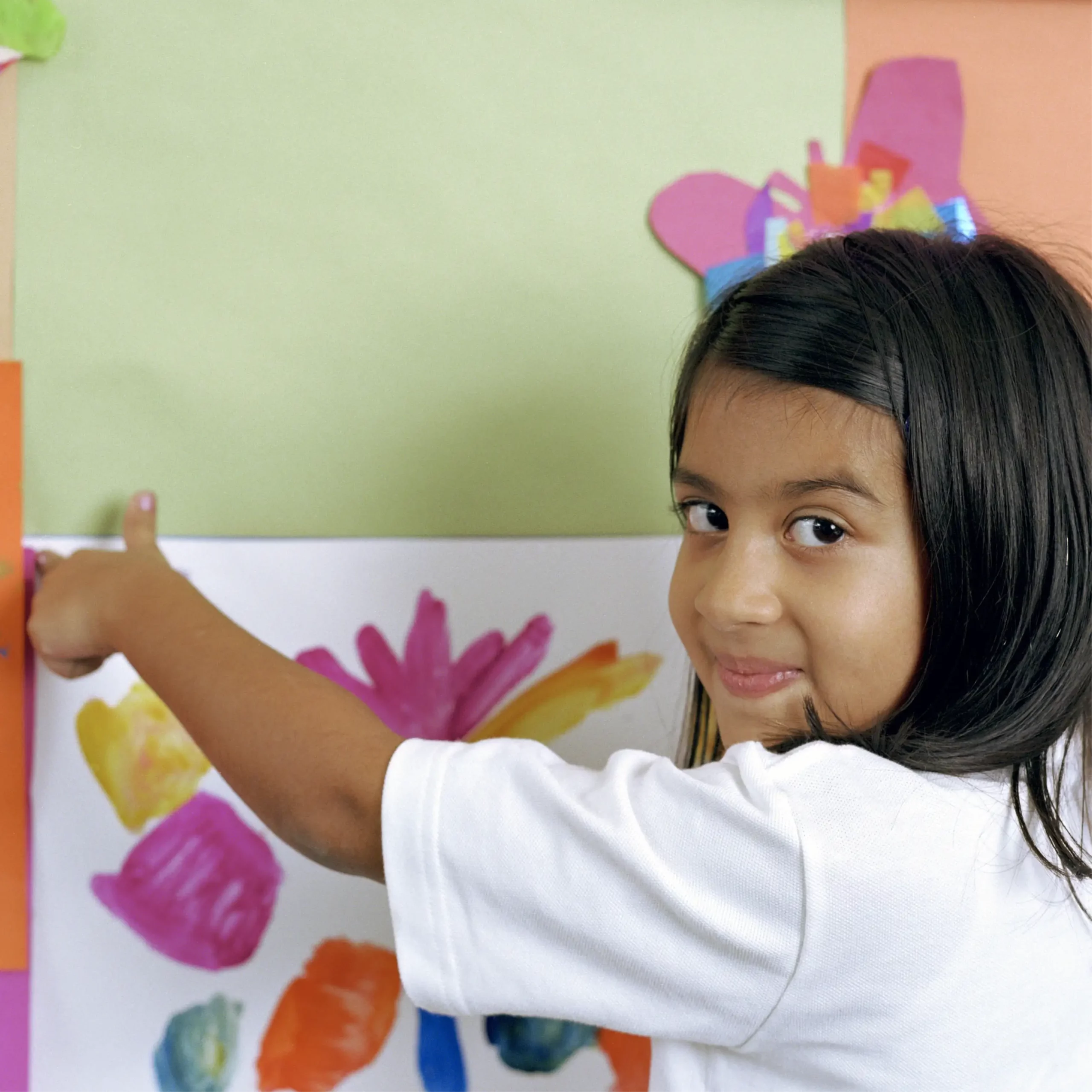 Smiling child points to their colourful painting displayed on a classroom wall.