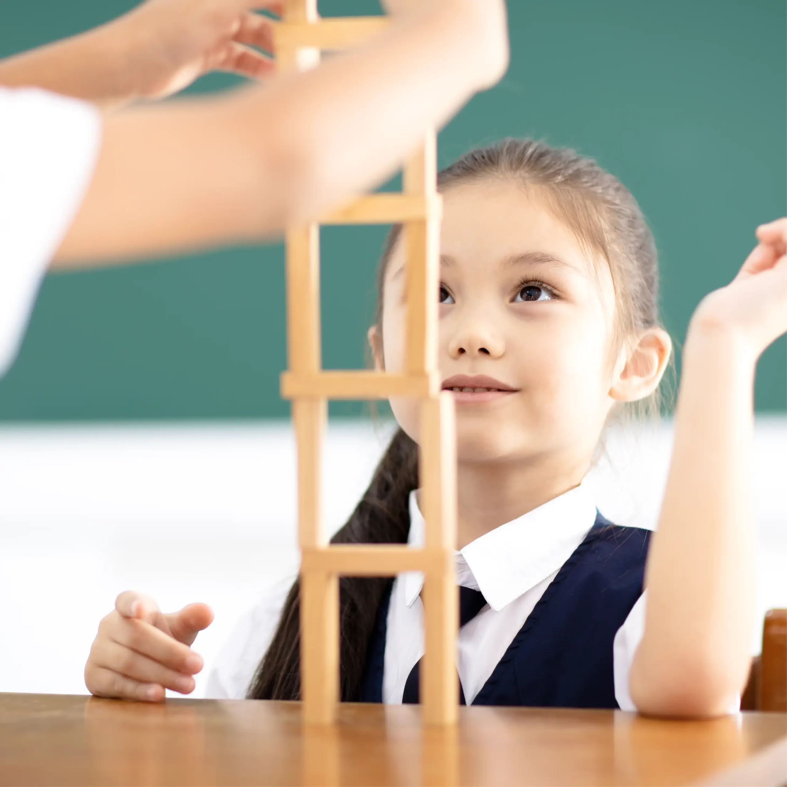 Girl in school uniform smiling while building a tall tower from wooden blocks.