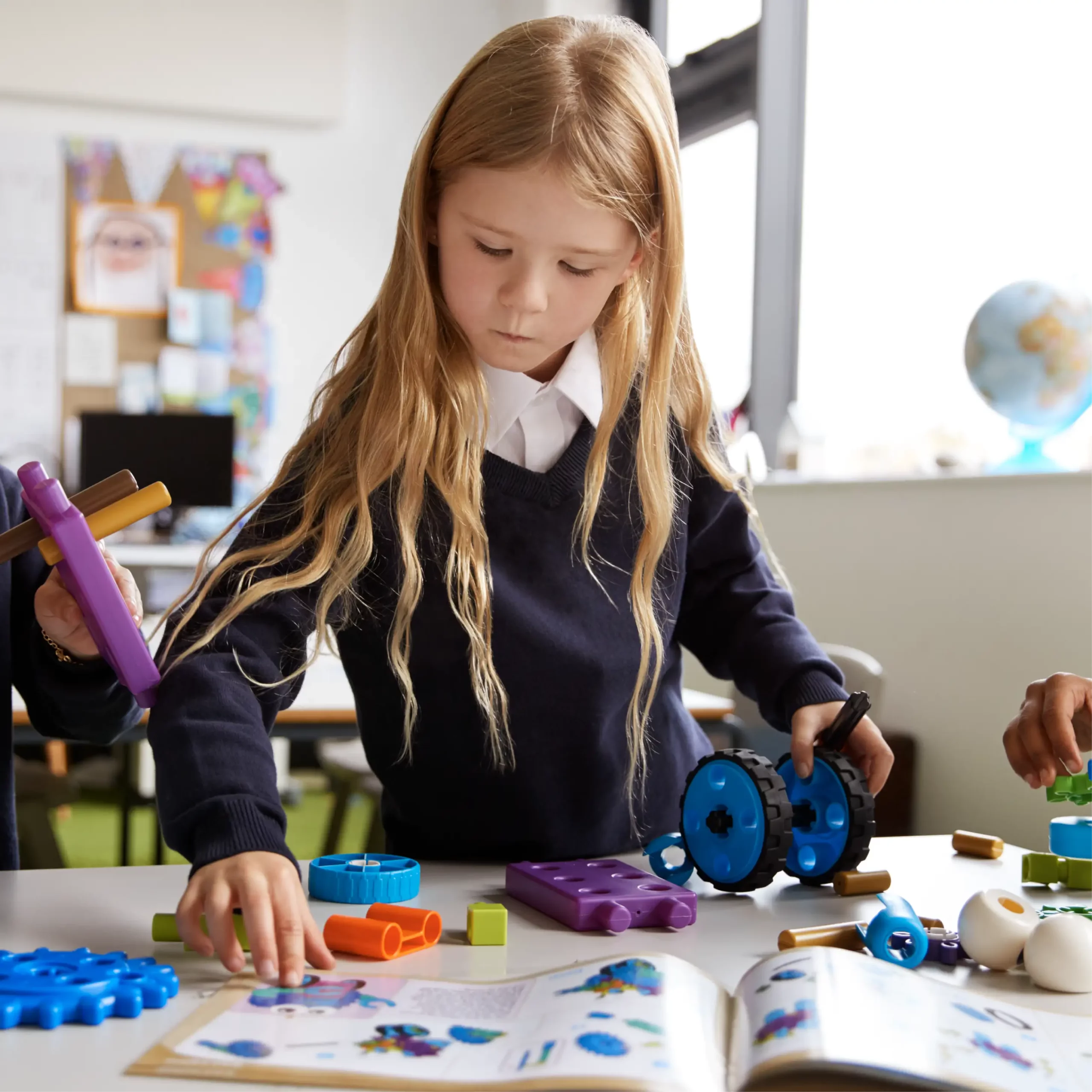Child building with colourful plastic gears and wheels while following instructions in a book.