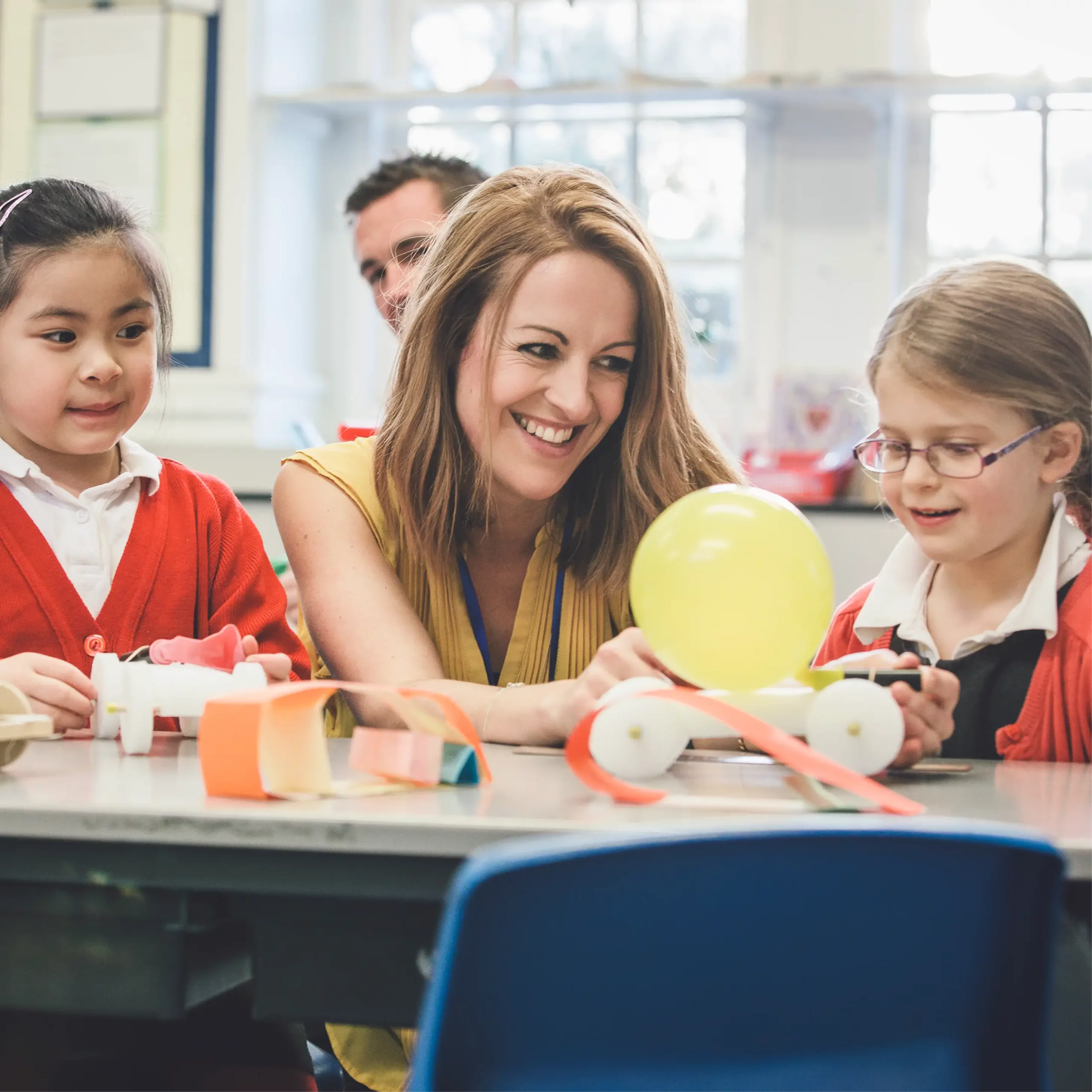 Teacher and two pupils smiling while working on a balloon-powered car project in class.