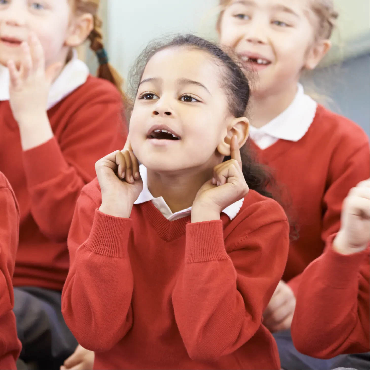 A group of young children in red school uniforms participating in a classroom activity