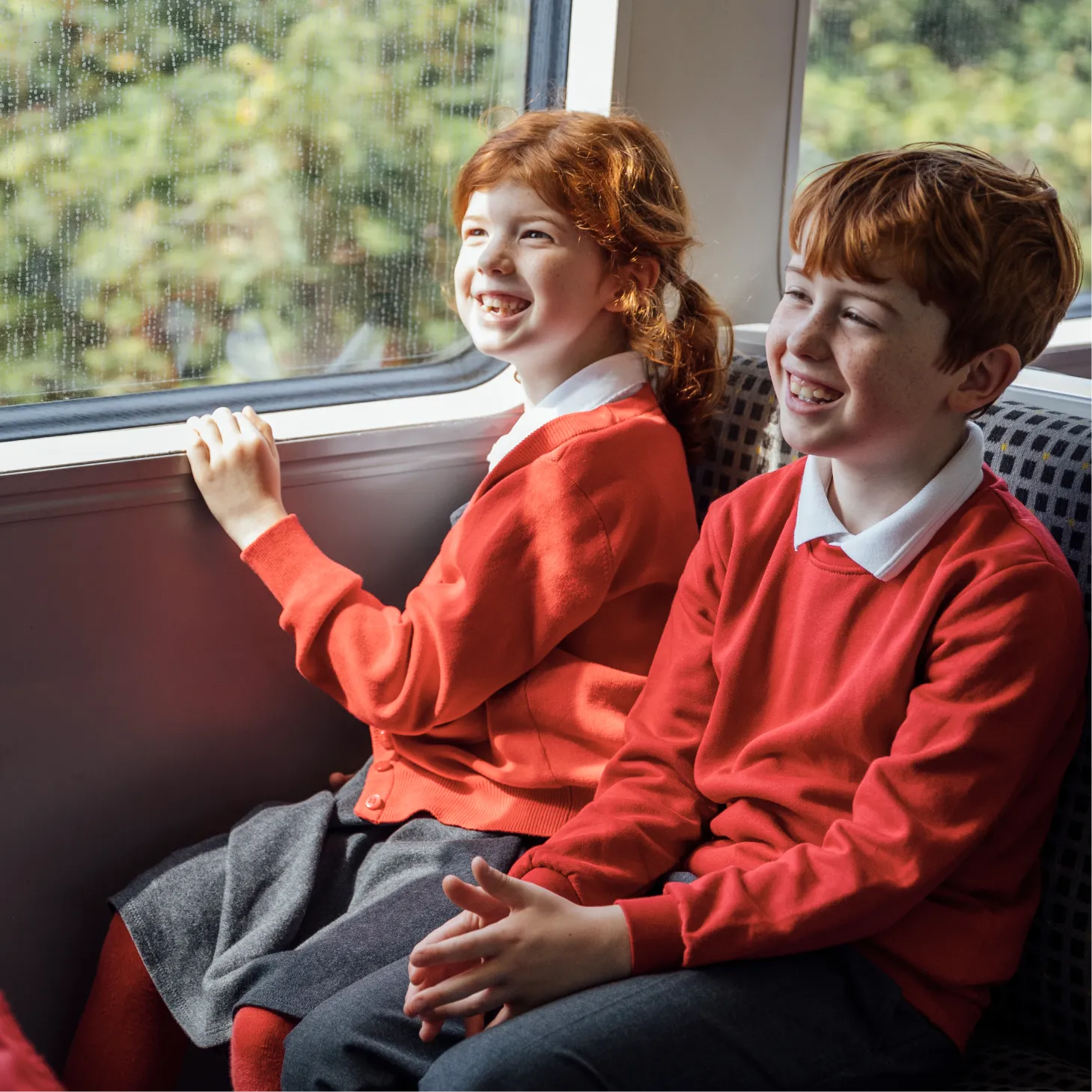 Two school children smiling and looking out of a train window