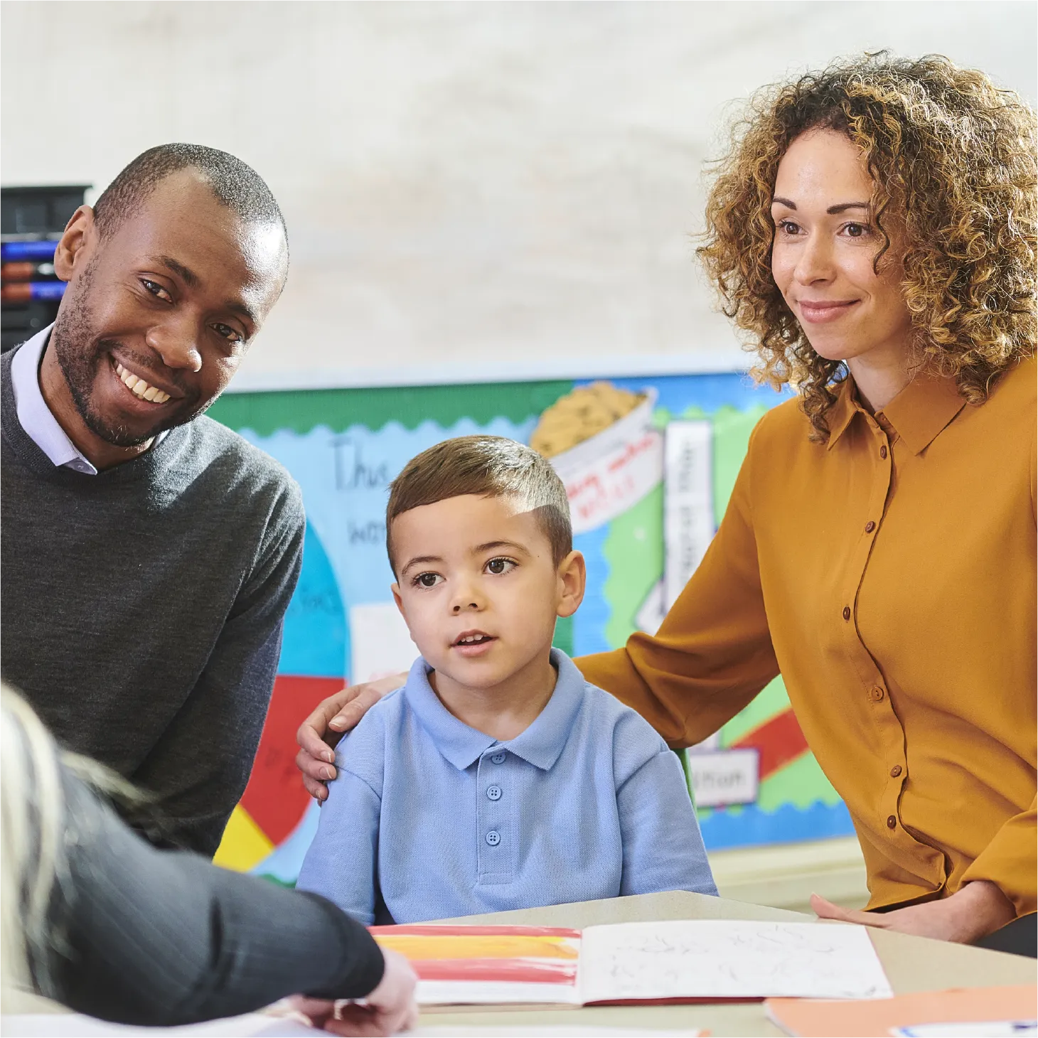 Parents and teacher talking with a young pupil about their work during a school meeting