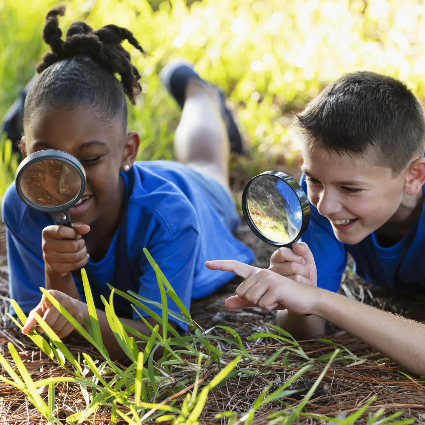 Two children using magnifying glasses to explore nature outdoors.