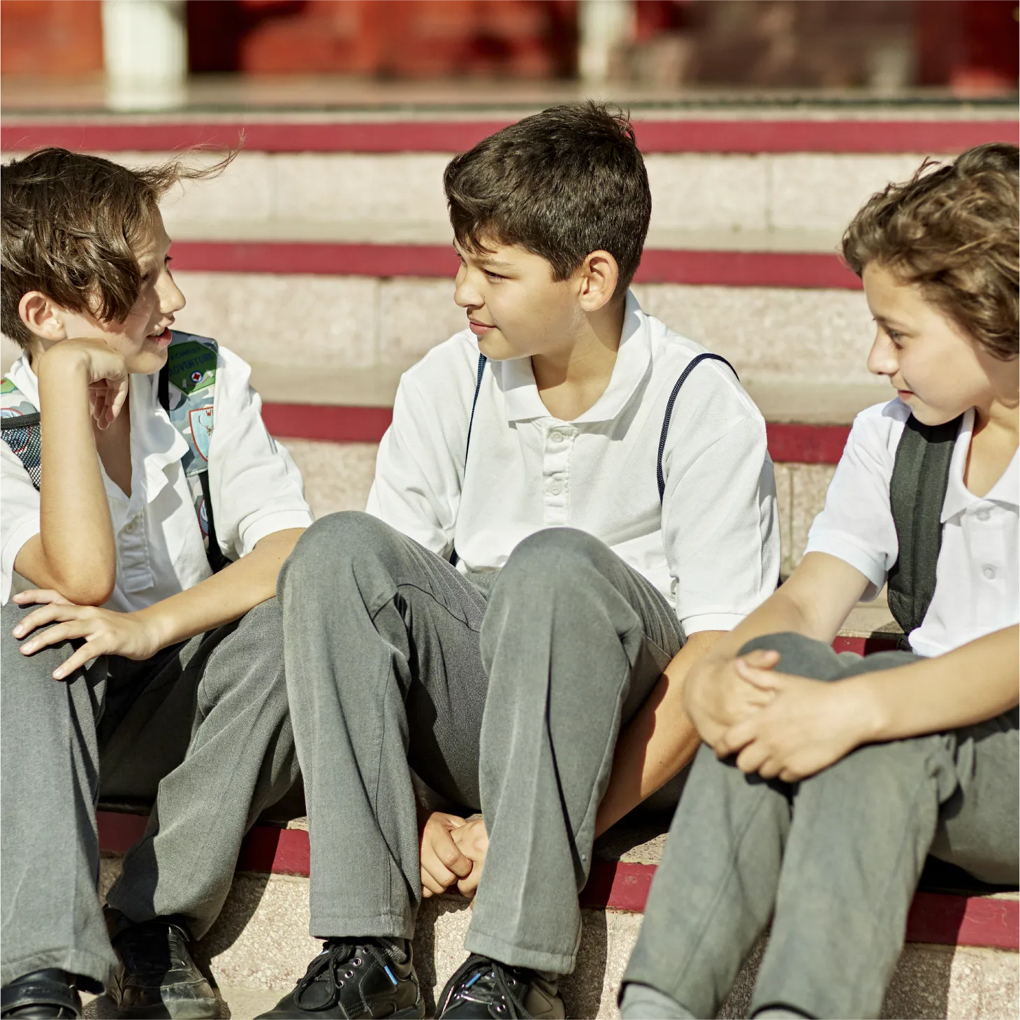Three schoolboys in uniform sitting on outdoor steps talking together.