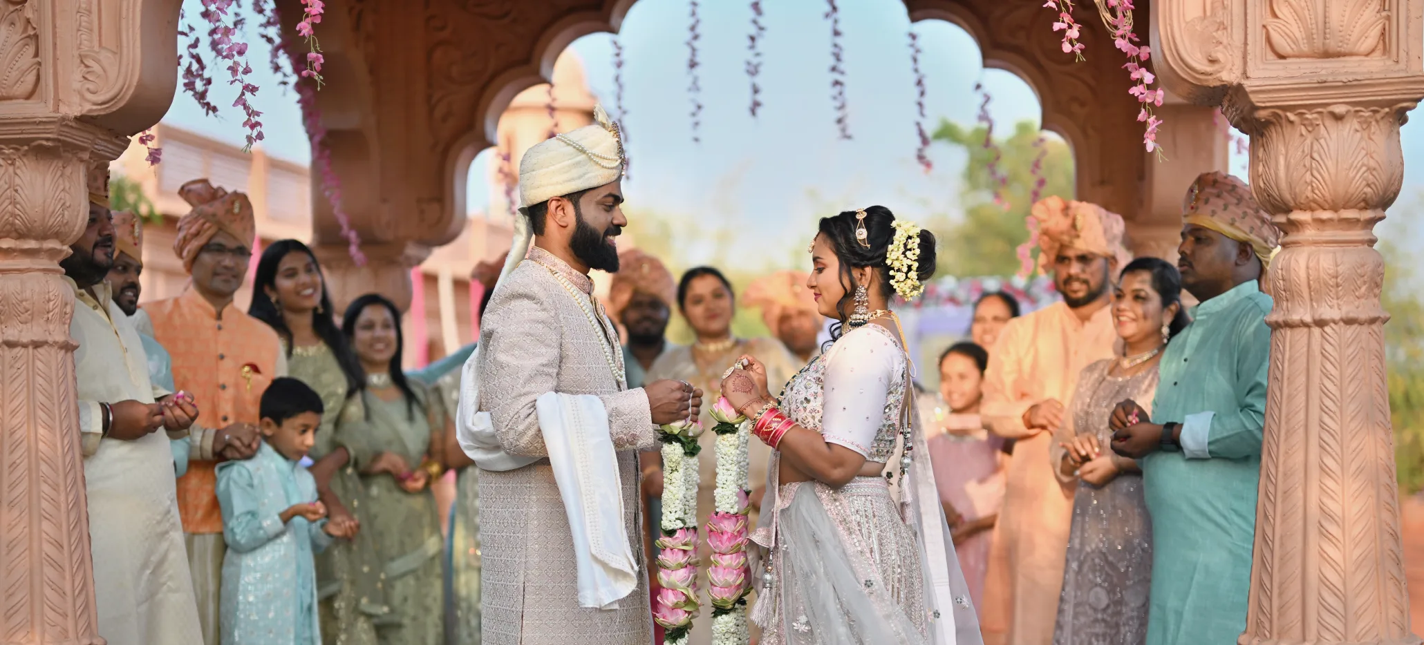 A couple taking part in a traditional wedding ceremony under a decorated arch, surrounded by guests.