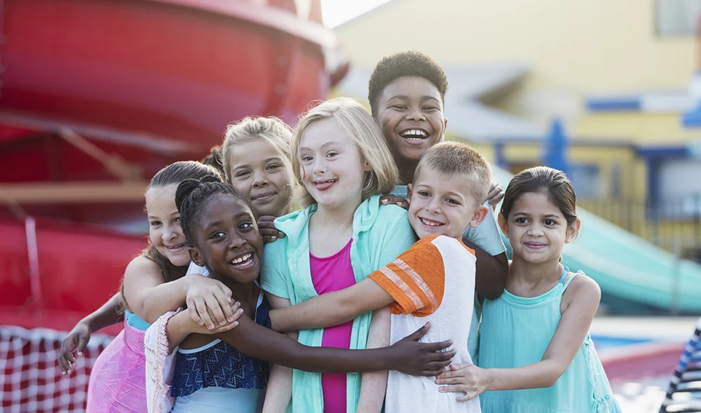 A diverse group of smiling children standing close together with their arms around each other, showing friendship and inclusion.