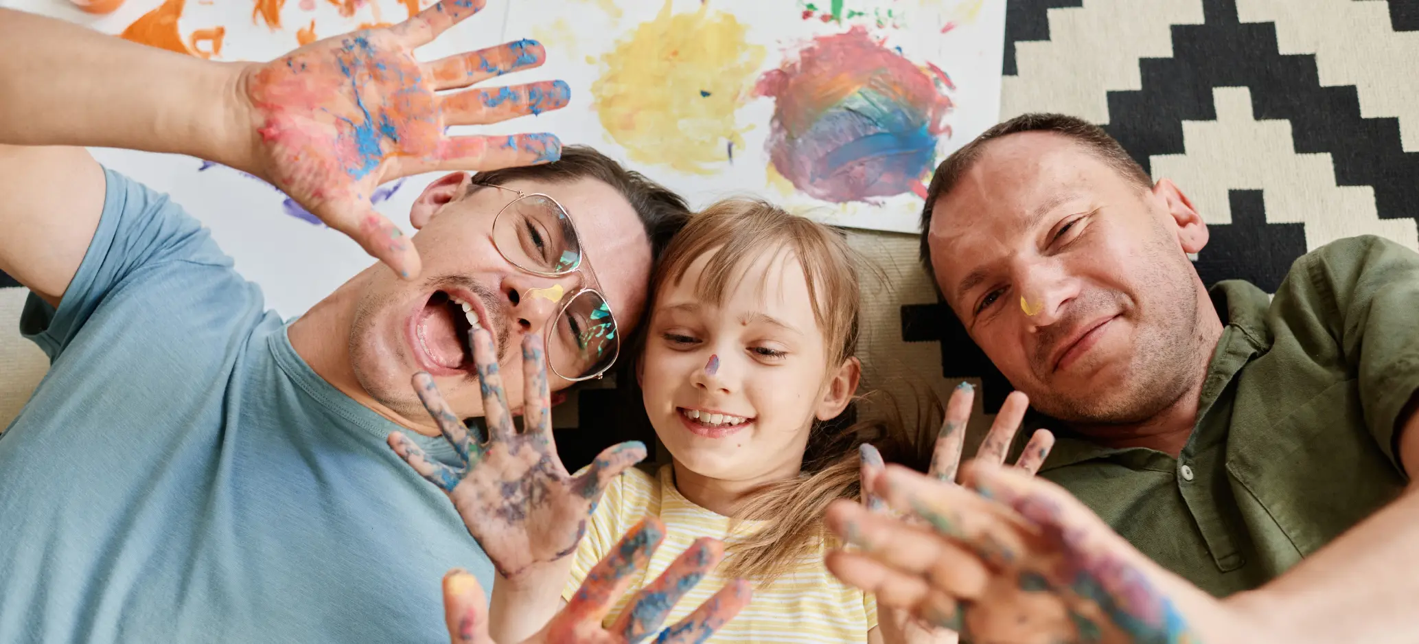 Parents and child smiling with paint-covered hands during creative play.