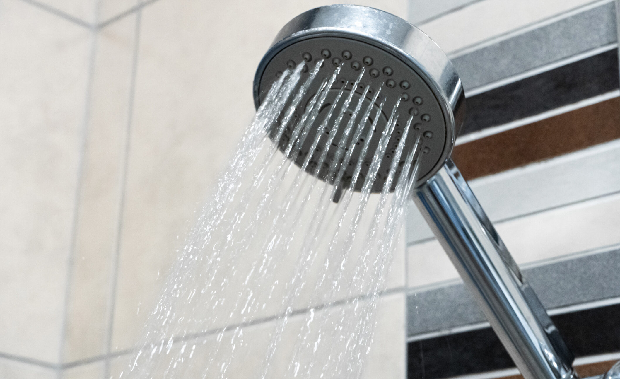 Shower head spraying running water in a tiled bathroom.