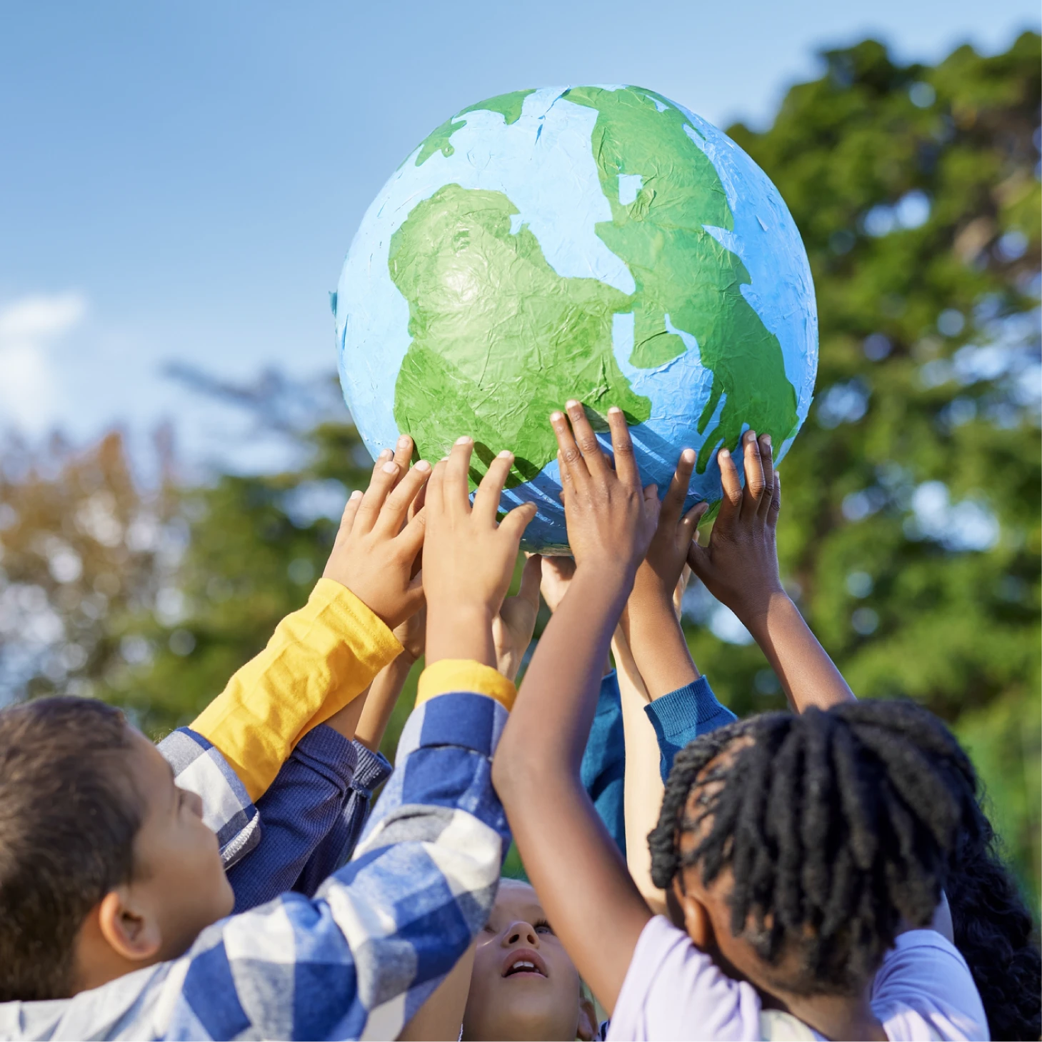 A group of children outdoors holding up a handmade globe together, showing teamwork and care for the planet.