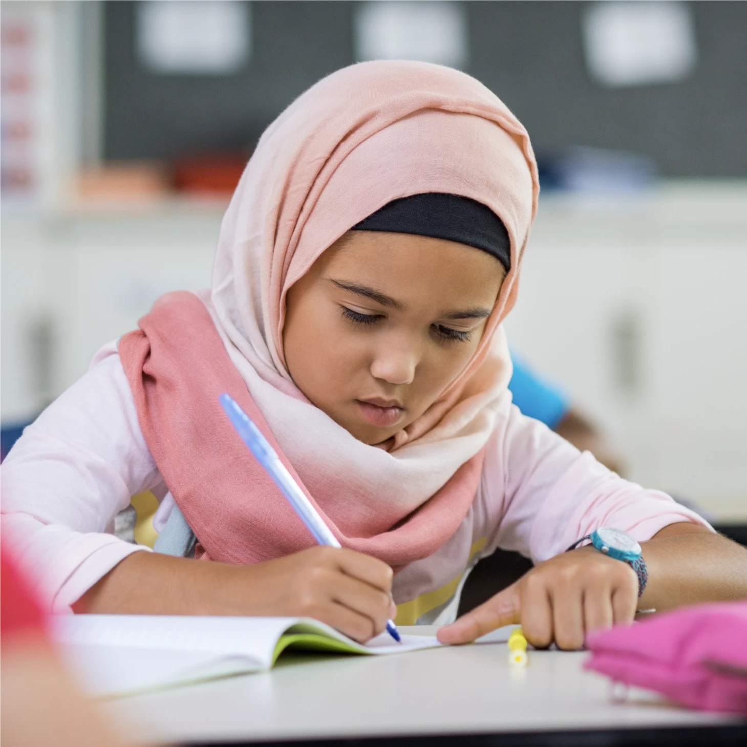 A young girl concentrating on her writing in class, with her head down facing her exercise book.